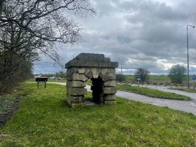 A stone structure in a grassy area
Description automatically generated